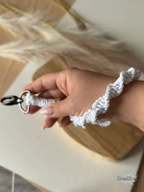 Macramé klíčenka Twist v bílé barvě se stříbrnou nitkou se silnější karabinou na ruce.