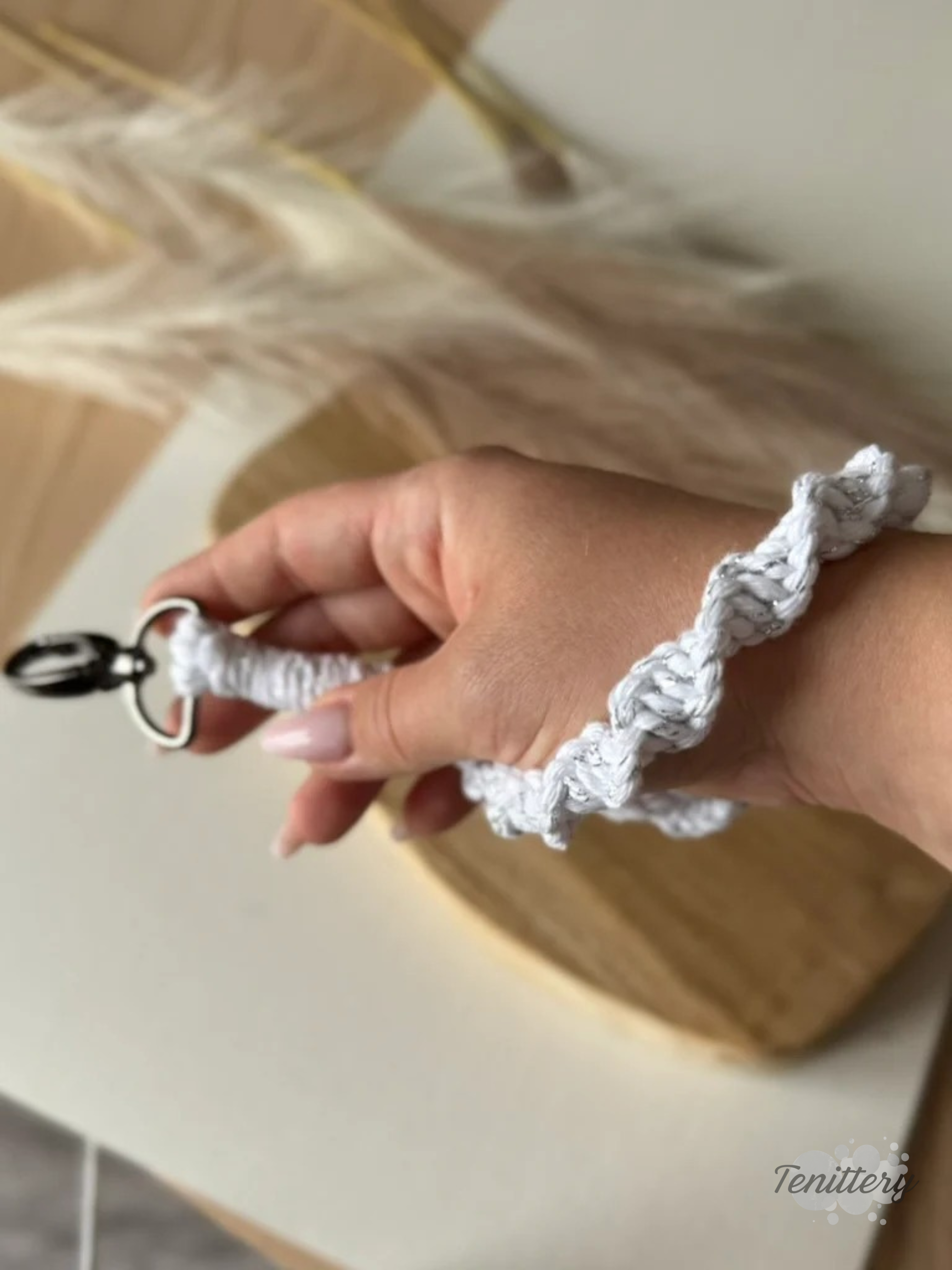 Macramé klíčenka Twist v bílé barvě se stříbrnou nitkou se silnější karabinou na ruce.
