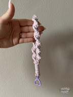 Macramé klíčenka Twist v žíhané růžové barvě s růžovou třpytivou nitkou s karabinou ve tvaru srdce v barvě lila - v ruce.